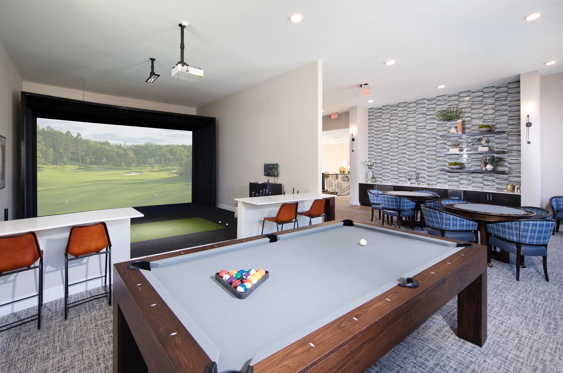 a game room with a golf simulator, pool table, and card tables with chairs at a senior apartment community